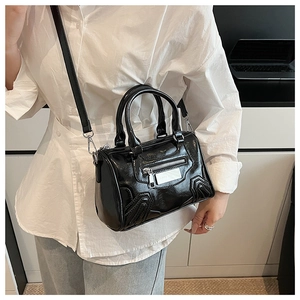 Detalle del bolso Boston de cuero negro brillante con cremallera frontal y placa metálica