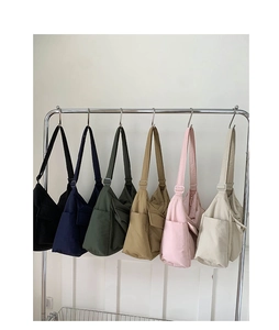 Detail showing various colors of canvas shoulder bags with adjustable straps on a rack