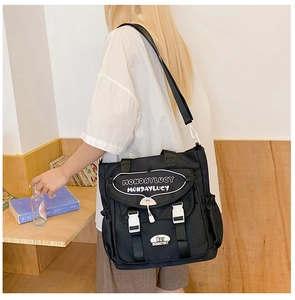 Detail of black canvas tote bag showing white buckles, drawstrings, and flap pocket