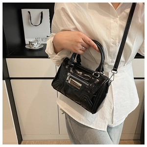 Detalle de un bolso cilíndrico de charol negro con placa metálica Lazy Breeze