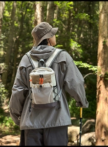 Detailed view of hiking backpack with mesh pocket and orange zippers in forest setting