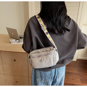 Detail of light grey nylon crossbody bag with multi-zipper layers and colorful floral strap