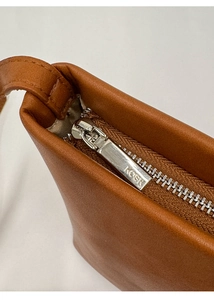 Detail of brown leather bucket bag showing fine texture and silver zipper with KOSK logo