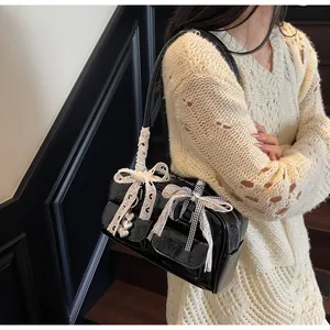 Detail of black patent leather bag featuring white lace bow and heart metal pendant