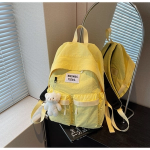 Dettaglio di uno zaino in nylon giallo con due tasche anteriori e un ciondolo a orsetto