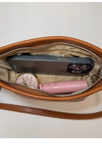 Interior storage space of the brown leather bucket bag showing phone and cosmetics