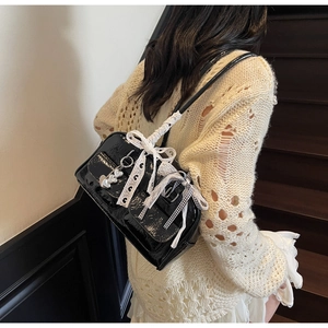 Detail of black patent leather shoulder bag with white lace bows and heart charms