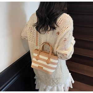 Detail of a striped knit bucket bag with brown leather handles and a detachable strap