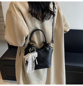 Détail du sac seau noir avec breloque élégante en perles et nœud en dentelle délicate