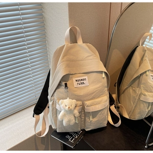 Dettaglio dello zaino in tela crema con tasche funzionali e ciondolo a forma di orso di peluche