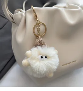 Close-up of a white fluffy monster charm with a brown knit hat on a beige leather bag