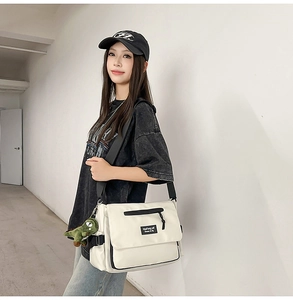 Detail of off-white canvas messenger bag with black strap and green dinosaur pendant