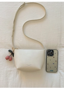 Close-up of cream white crescent crossbody bag with cherry charm and brand logo