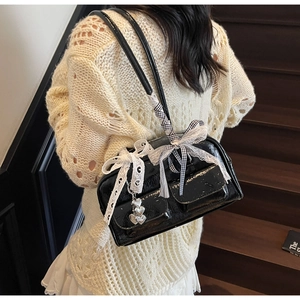 Close-up of black patent leather bag with white lace bow and silver heart charm