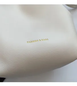Close-up of off-white leather texture with gold lettering on stylish bucket bag