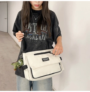 White canvas messenger bag featuring multiple compartments and a green dinosaur pendant