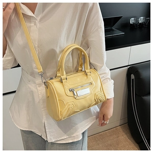 Detalle de bolso Boston amarillo pálido con cremalleras plateadas y textura brillante