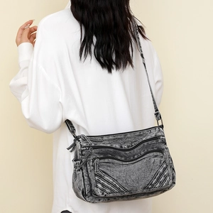 Detail of grey washed denim tote showing multi-zipper pockets and black fabric strap