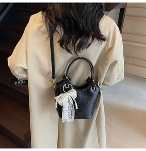 Détail du sac seau noir avec nœud en dentelle blanche sur un modèle en trench beige
