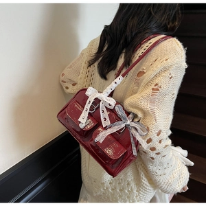 Deep red patent leather shoulder bag with lace bow details on a model
