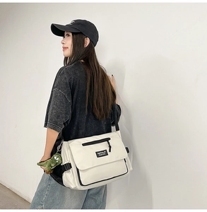 Detail of off-white canvas messenger bag with brand label and cute green dinosaur charm