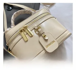 Detailed close-up of cream box bag with gold zippers and purple scarf handle