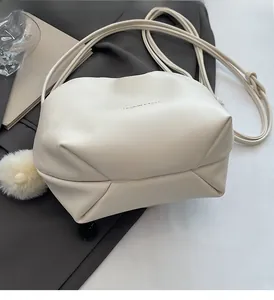 Detail of creamy white pleated shoulder bag with plush ball charm on a grey blazer