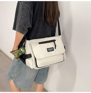 Detailed side view of white canvas messenger bag with black strap and green dinosaur charm