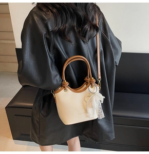 Détail d'un sac seau crème avec bordure marron et nœud en dentelle sur veste en cuir
