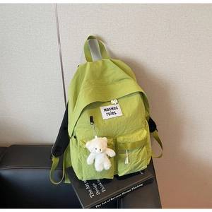 Dettaglio zaino in nylon verde lime con tasche frontali e ciondolo a forma di orsetto