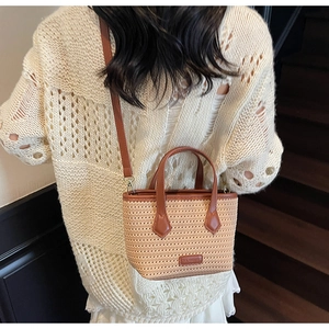 Close-up of beige knitted bucket bag with brown leather handles and adjustable strap