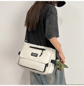 Detail view of off-white nylon messenger bag featuring a green dinosaur plush keychain