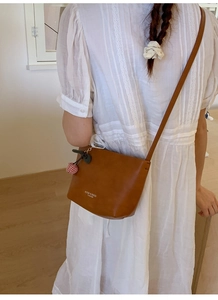 Detail of brown leather bucket bag with cherry charm and white brand lettering on side