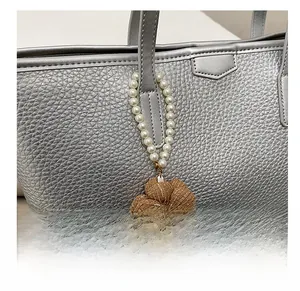 Détail du charme de fleur avec perles blanches et tissu rayé marron sur un sac argenté