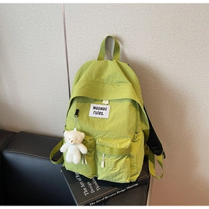 Dettaglio dello zaino in nylon verde avocado con tasche frontali e ciondolo orso