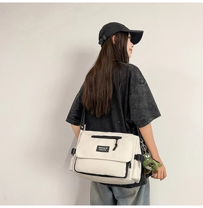 Detail of off-white crossbody messenger bag with side dinosaur plush toy and flap pockets