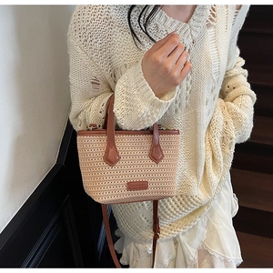 Detail of woven straw bucket bag with brown leather trim and adjustable shoulder strap