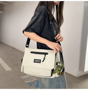 White canvas messenger bag with contrast trim and cute green dinosaur plush charm detail