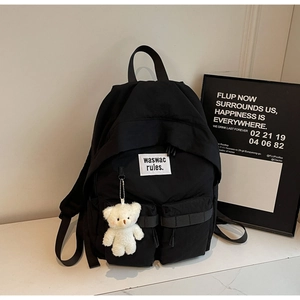 Dettaglio di uno zaino in tela nera con due tasche frontali e portachiavi a forma di orso