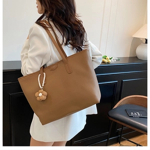 Sac cabas marron grainé avec pendentif floral et perle porté par un mannequin