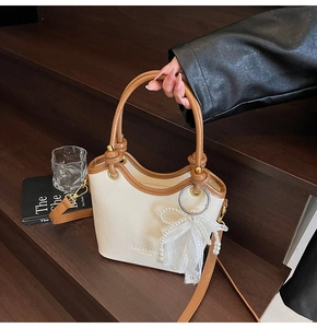 Détail du sac seau crème avec poignées marron et accessoire de nœud en dentelle et perles
