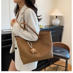 Sac fourre-tout marron caramel avec pendentif fleur de perle élégant porté par un mannequin