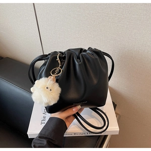 Detail of black pleated drawstring bucket bag with white plush charm on books