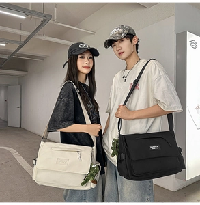 Detail of canvas messenger bags in beige and black with adjustable straps and dinosaur charm