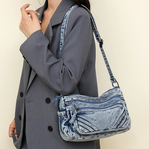 Detail view of denim crossbody bag with multiple zippers and adjustable shoulder strap