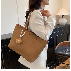 Sac cabas en cuir marron avec breloque fleur et perle porté par un mannequin en costume