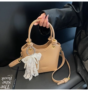 Détail du sac seau en cuir beige avec nœud en dentelle et perles, texture grainée