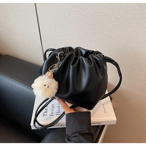 Detail of black faux leather bucket bag featuring a white fuzzy pom-pom charm and drawstrings