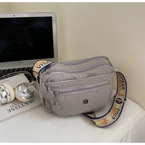 Detail of grey oxford fabric crossbody bag showing multi-layered zippers and shoulder strap