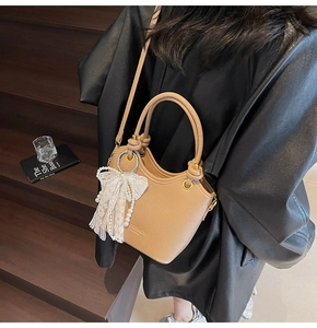 Détail du sac seau en cuir kaki avec un nœud en dentelle blanche et pendentif perle